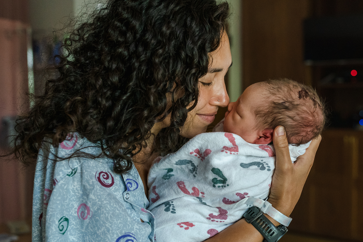A mother with brown hair nose to nose with an infant