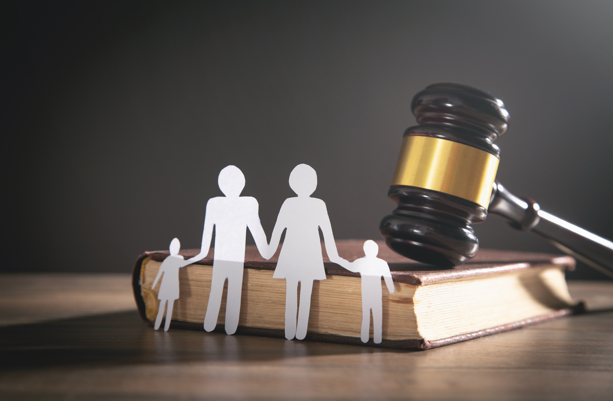 Paper cutouts of a family in front of a book with a courtroom gavel on top of it.