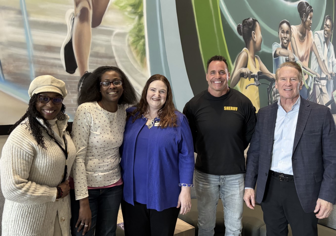 Five people standing side by side and smiling in front of a mural