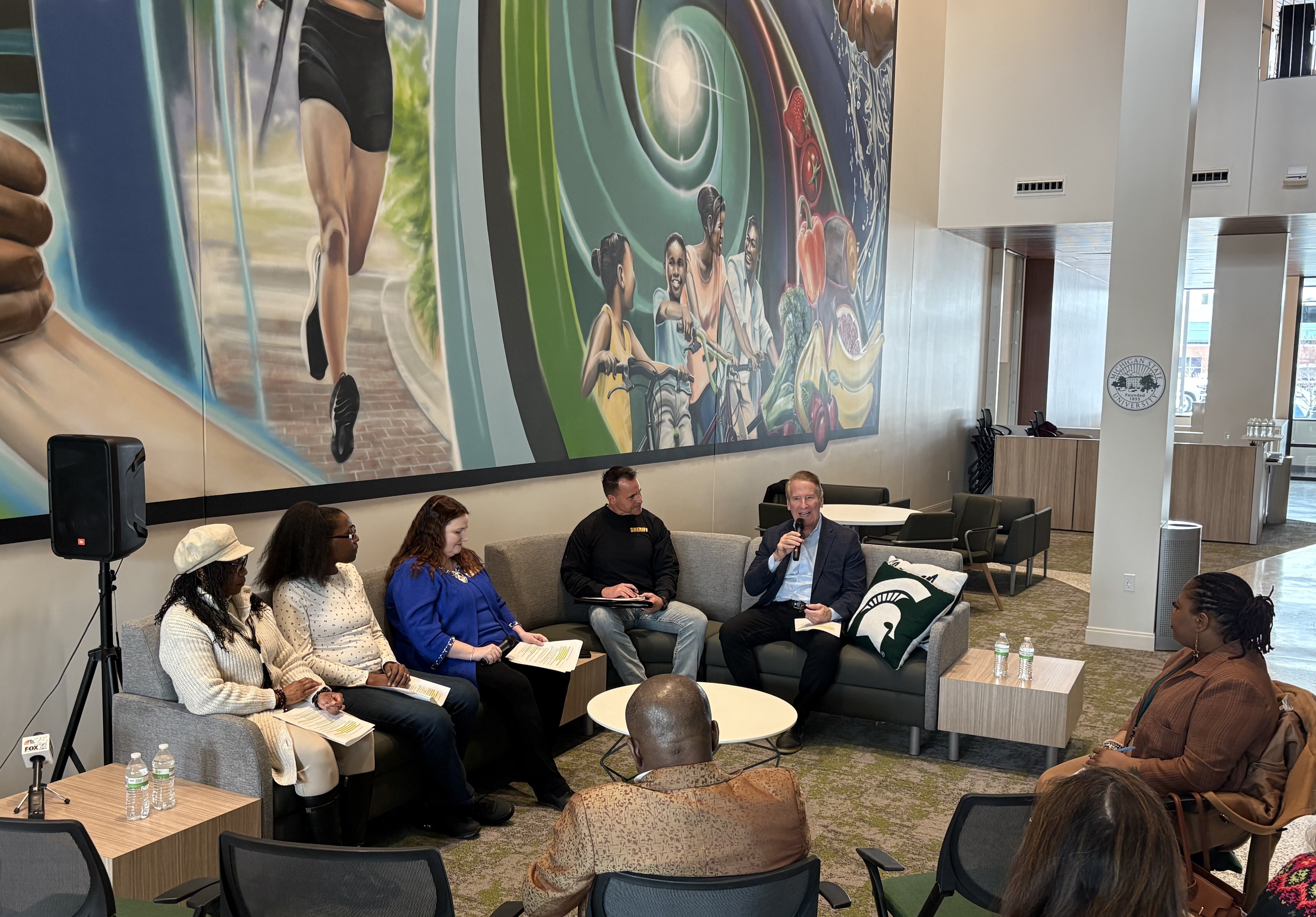 Three women and two men on a couch with microphones in front of a mural.